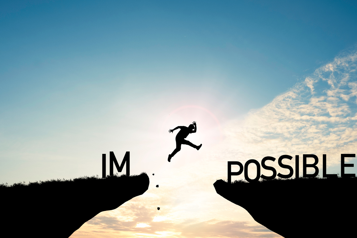 Mindset concept ,Silhouette man jumping over impossible and possible  wording on cliff with cloud sky and sunlight.